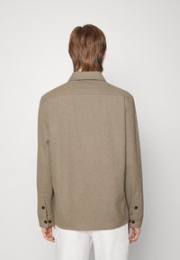 Olivengroene, wollen overhemdjas met een puntige kraag, lange mouwen en zwarte knoopaccenten op de manchetten. Eenvoudig ontwerp, zonder zichtbare patronen.