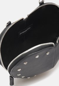 Borsa rotonda nera con accenti di borchie metalliche, texture liscia, chiusura con zip e interno in tessuto con etichetta del marchio.