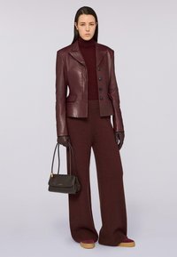 Giacca in pelle borgogna con vestibilità sartoriale e bottoni prominenti, abbinata a pantaloni larghi borgogna, guanti neri e una piccola borsa scura.