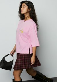 Lyserød oversize t-shirt med sideskår, med blomsterbroderi, stylet med en flared brun ternet nederdel og sort håndtaske.