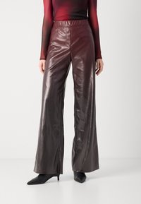 Bordeaux leren wijde broek met een hoge taille en een subtiele glans. Voorzien van zijzakken en een ontspannen pasvorm, gecombineerd met zwarte schoenen.