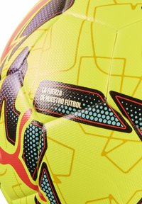 Gul og flerfarvet mønstrede fodbold med tekstureret overflade og spansk tekst "La fuerza de nuestro fútbol" på panelet.