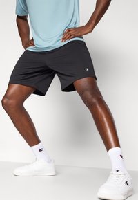 Μαύρα αθλητικά σορτς με άνετη εφαρμογή, συνδυασμένα με ανοιχτό μπλε πουκάμισο και λευκά αθλητικά παπούτσια. Διαθέτουν λογότυπο Champion στα σορτς και τις κάλτσες.