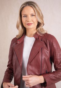 Burgundy leather motorcycle jacket with quilted shoulder accents, zippered pockets, and a notched collar, worn over a white shirt.