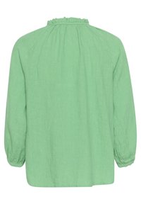 Grüne Leinenbluse mit rüschigem Ausschnitt, langen Ärmeln mit elastischen Bündchen und einem lockeren Schnitt. Texturiert mit einem weichen Fall.