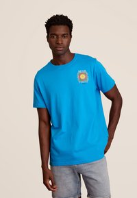 Felblau katoenen t-shirt met korte mouwen, voorzien van een bedrukking op de linker borst en een ronde hals. Casual pasvorm.