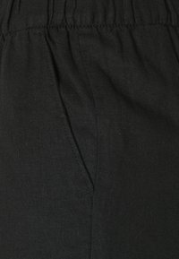 Pantalones de lino negros con una cintura fruncida, bolsillo lateral y superficie texturizada. La tela parece ligera y transpirable.