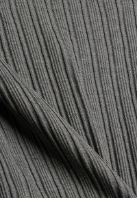 Grå ribbad tyg med vertikala linjer, som visar en mjuk textur och sömlös konstruktion, hängande i en naturlig veck.