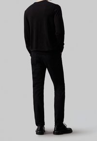 Zwarte gebreide trui met lange mouwen, gecombineerd met zwarte slim-fit jeans en glanzende zwarte schoenen, gezien van achteren. Eenvoudig en naadloos ontwerp.