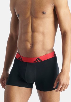 Boxer ajustados negros con una cintura elástica roja que presenta logotipos negros de Adidas. La tela parece suave con un diseño entallado.