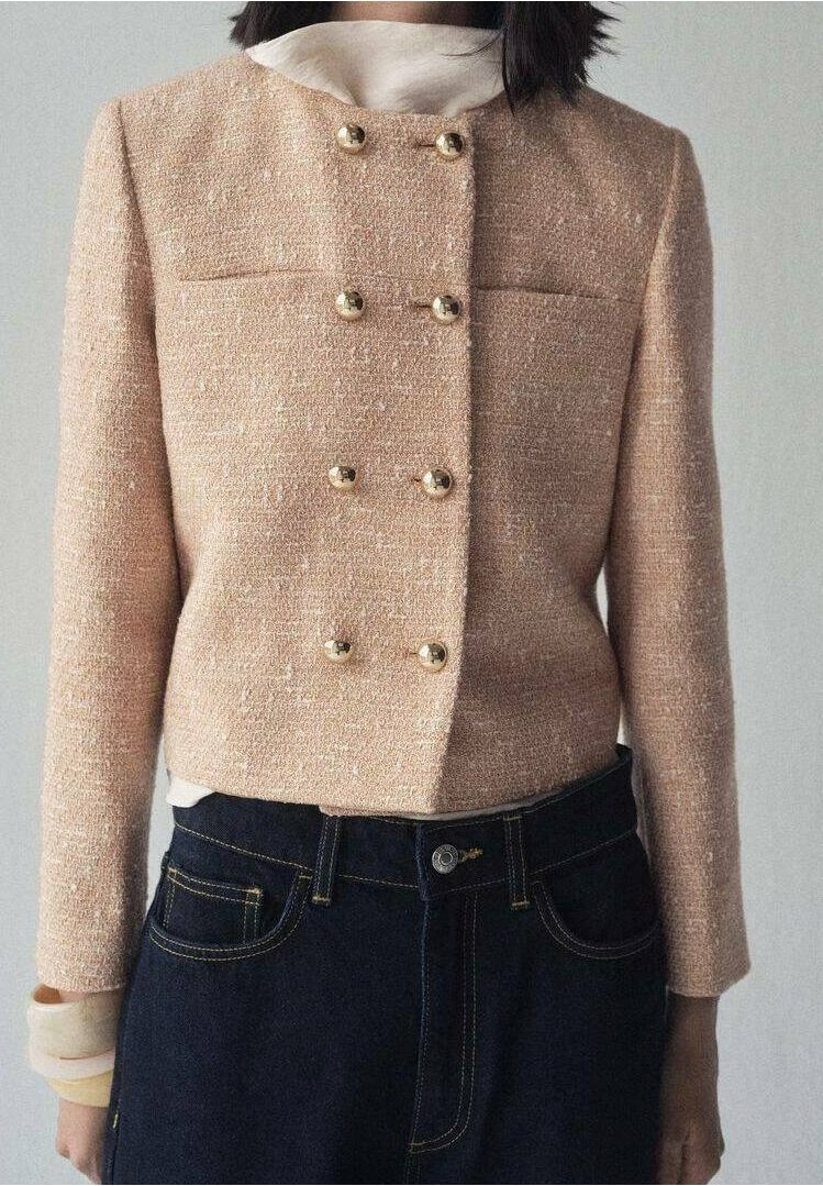Femme portant une veste texturée rose clair croisée à boutons dorés, par-dessus un haut blanc et un jean foncé taille haute.