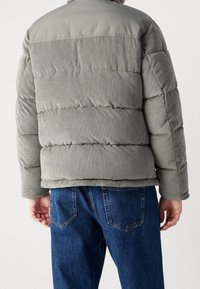 Szara kurtka puchowa z prążkowaną fakturą na plecach i gładkim materiałem na ramionach. Połączona z ciemnoniebieskimi dżinsami.