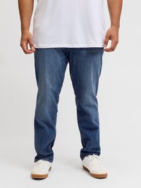 Μπλε τζιν παντελόνι με ίσια γραμμή, που διαθέτει διακριτικά ξεθωριάσματα και κλασικό σχέδιο πέντε τσεπών. Φοριέται με λευκά αθλητικά παπούτσια.