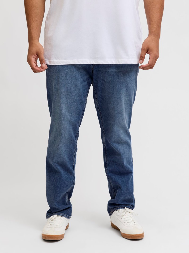 Μπλε τζιν παντελόνι με ίσια γραμμή, που διαθέτει διακριτικά ξεθωριάσματα και κλασικό σχέδιο πέντε τσεπών. Φοριέται με λευκά αθλητικά παπούτσια.