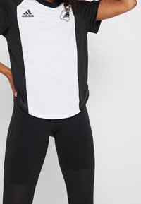 Černo-bílý atletický dres s krátkými rukávy, na levé hrudi s logem Adidas a s kontrastními bočními panely.