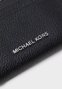 Svart skinnlommebok med teksturert overflate og sølvfarget "MICHAEL KORS"-logo. Kompakt design med flere kortlommer.
