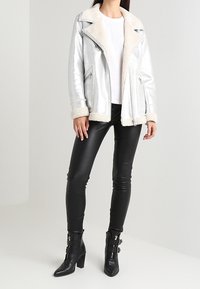 Giacca in finta pelle argentata metallizzata con colletto e polsini in sherpa crema, abbinata a leggings in finta pelle nera e stivaletti con fibbie.
