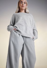 Ljusgrå stickad tröja med avslappnad passform och ribbade muddar, kombinerad med grå randiga vida byxor; mjuk textur, avslappnad stil.