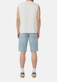 Chemise sans manches blanche, shorts en denim bleu clair, chaussures décontractées avec des accents blancs et navy, détails de poches arrière visibles.