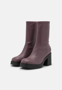 Botines de cuero púrpura con un diseño ajustado, punta redonda y un tacón grueso negro. Presenta costuras visibles y una textura suave.