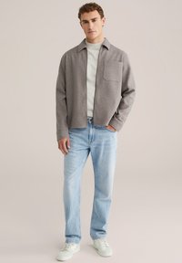 Grijs colbert over een lichte trui, gecombineerd met lichtblauwe spijkerbroeken en witte sneakers; heeft een borstzak en een relaxte pasvorm.