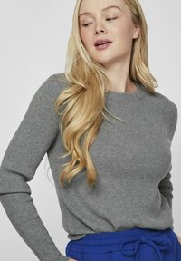 Suéter gris de canalé con cuello redondo y mangas largas. La tela parece suave. Combinado con pantalones azul con cordón.