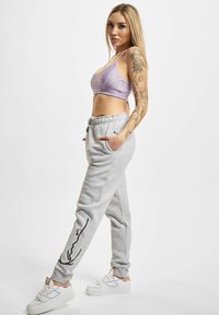Grå joggebukser med slim fit, med en sidelomme og et svart linjedesign. Kombinert med en lavendel kuttet idrettstopp og hvite joggesko.