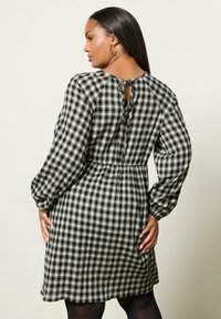 Schwarz-weiß karierter Kleid mit gerafftem Bund, langen Puffärmeln und einer geknöpften Rückenöffnung, aus leichtem Stoff gefertigt.