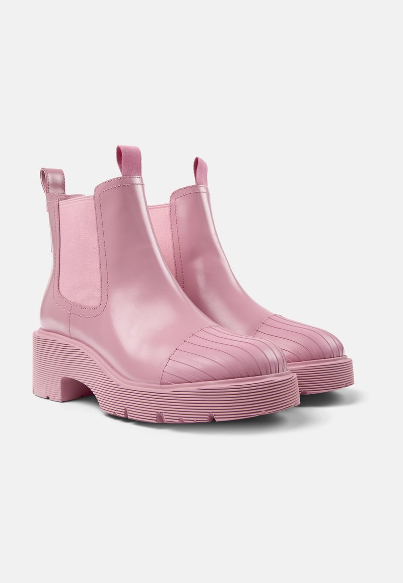 Une paire de bottines Chelsea en cuir rose avec des semelles épaisses à nervures et des panneaux élastiques sur les côtés, présentée à un léger angle sur un fond blanc.