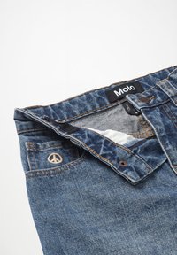 Denim kratke hlače z temno modrim pranjem, ki imajo vezenino znaka miru na žepu, kontrastno šivanje in blagovno ime na notranji strani pasu.