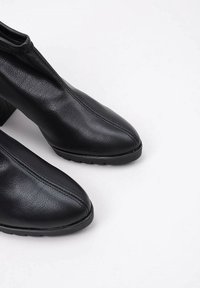 Black leather ankle boots with a sleek design, pointed toe, side zip closure, and textured finish. Low block heels add stability.