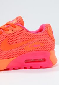 Baskets Nike Air Max en mesh orange vif et rose, avec une unité Air visible, une semelle texturée et un logo proéminent sur le côté.