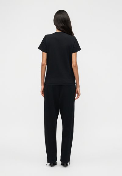 Μαύρο βαμβακερό T-shirt με κοντά μανίκια και άνετη εφαρμογή, συνδυασμένο με φαρδιά μαύρη παντελόνια και μυτερές μαύρες γόβες, που παρουσιάζει έναν μινιμαλιστικό σχεδιασμό.