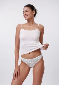 Biały bawełniany top na ramiączkach z cienkimi paskami oraz bikini z jasnym kwiatowym wzorem w kolorach niebieskim, żółtym i białym. Gładka tekstura, dopasowany fason.