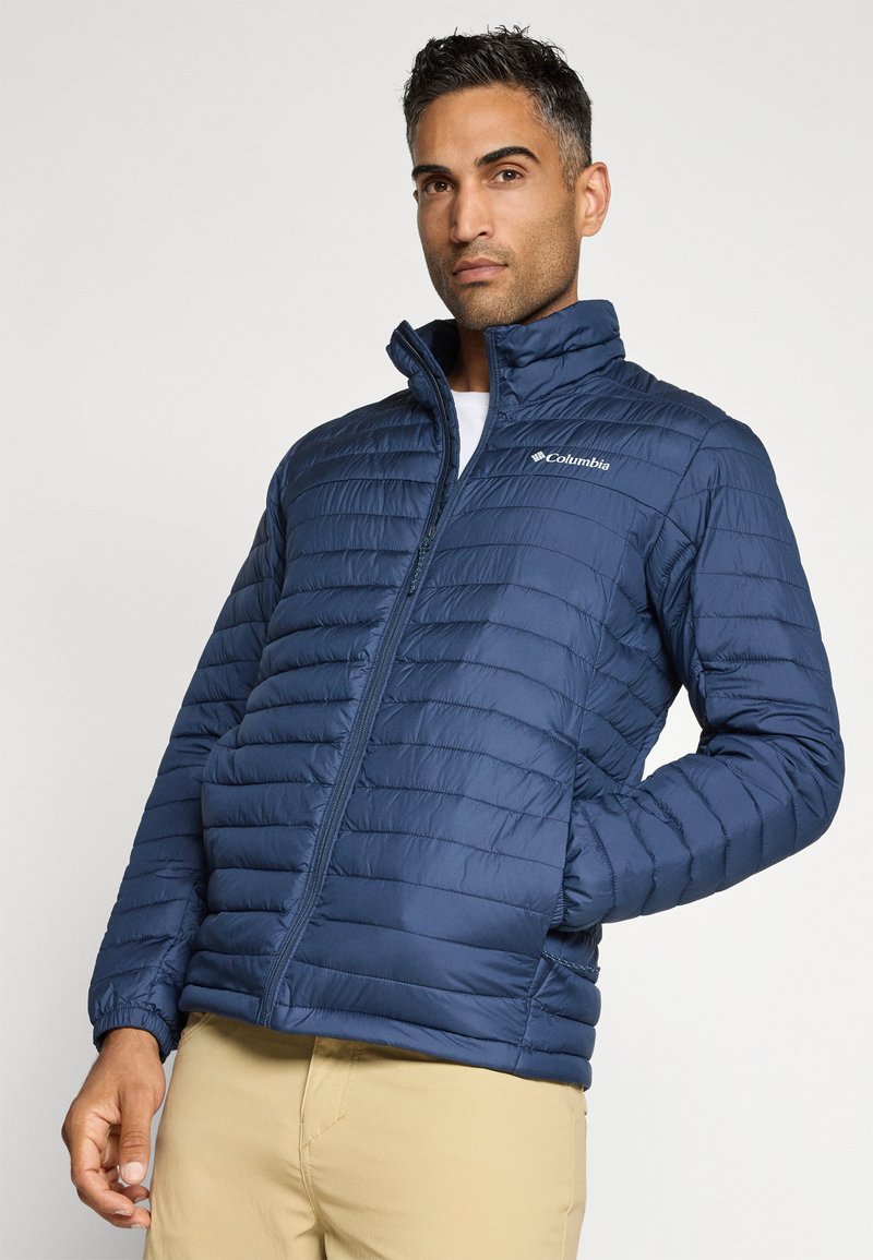 Veste rembourrée bleu marine avec une fermeture éclair intégrale, un col montant et un motif matelassé horizontal. Comprend le logo Columbia sur la zone gauche de la poitrine.