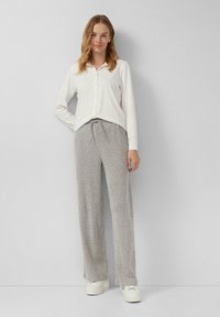 Langärmliges weißes Button-up-Hemd kombiniert mit hellgrauen gemusterten Lounge-Hosen, die einen elastischen Bund haben, und weißen Sneakers.