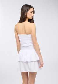 Abito bianco senza spalline con un corpetto arricciato e orlo a strati, realizzato in tessuto leggero, con un design testurizzato.