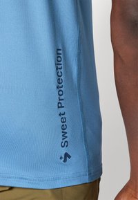 Jasnoniebieska koszulka sportowa o gładkiej fakturze, z granatowym nadrukiem logo z boku i kontrastowym szyciem. Krótkie rękawy, dopasowany krój.