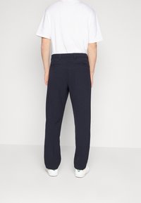 Pantalon bleu marine à coupe ajustée, avec un devant plat, des poches arrière et une texture lisse, associé à un t-shirt blanc à col rond.