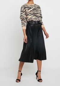 Beige tröja med svarta zebrarand, i kombination med en svart plisserad midikjol och svarta högklackade sandaletter. Kjolen har ett bälte.