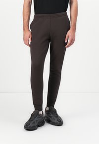 Braune, schmal zulaufende Jogginghose aus weichem Stoff mit elastischem Bund und Bündchen, kombiniert mit klobigen schwarzen Sportschuhen.