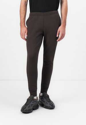 Brune tapered sweatpants lavet af blødt materiale med elastisk talje og manchetter, parret med klodsede sorte løbesko.