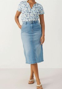 Vaaleansininen denim-midihame, jossa on edessä halkio, yhdistettynä lyhythihaiseen valkoiseen paitaan, jossa on sinisiä kukkakuviota. Asusteena beiget sandaalit.