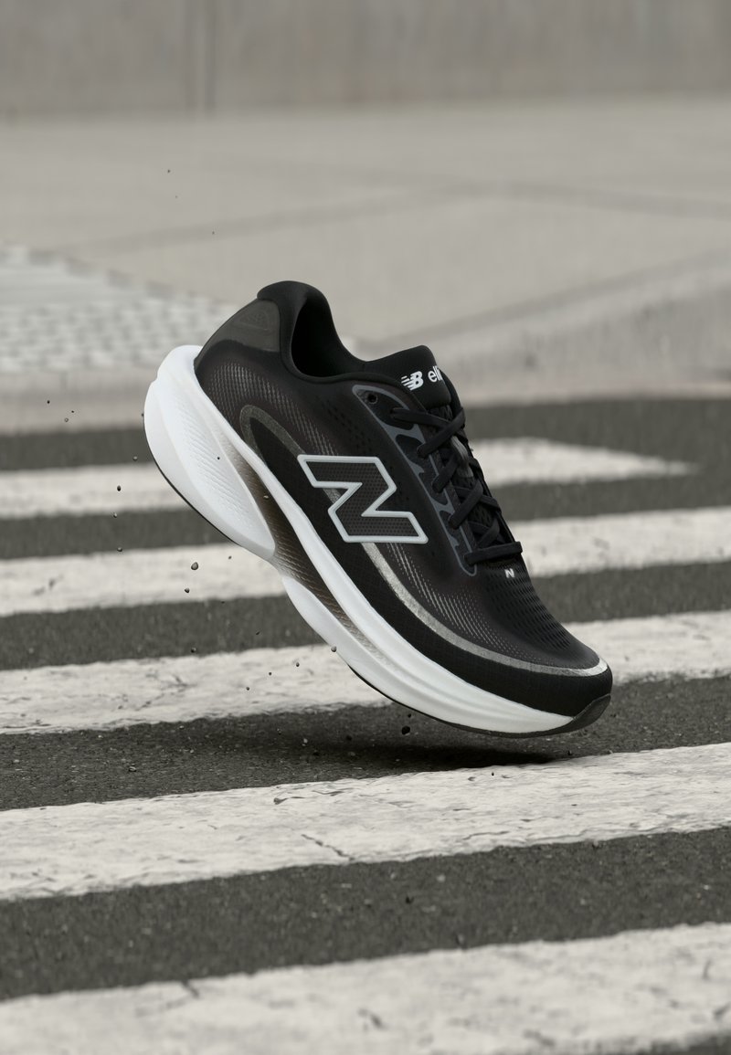 Scarpa da corsa New Balance in bianco e nero in aria sopra un attraversamento pedonale su una strada asfaltata.