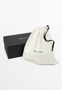 Snørelukket lærredstaske i cremefarve med sorte detaljer, suppleret med en elegant sort æske med "Massimo Dutti"-logo i hvid.