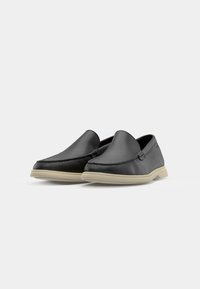 Black leather slip-on shoes with a smooth texture and a braided accent along the front, featuring a beige rubber sole.