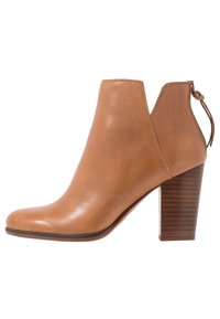 Stivale alla caviglia in pelle color senape con punta arrotondata, lati traforati e tacco testurizzato. Dotato di linguetta per facilitare la calzata e dettagli cuciti.