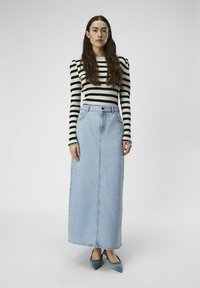 Striped black and white long-sleeve top paired with a light blue denim maxi skirt. Features a high waist and front pockets, complemented by blue high-heeled shoes.