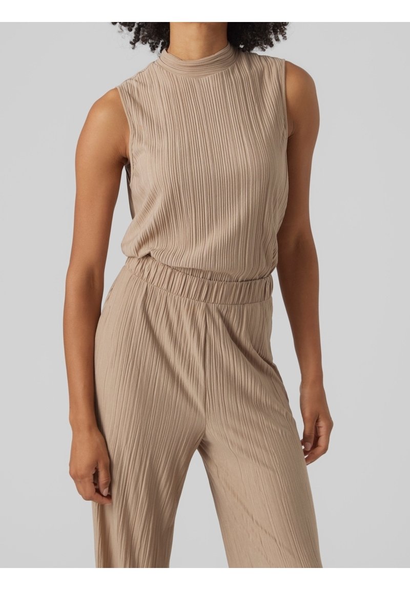 Haut beige côtelé sans manches et pantalon assorti avec taille élastique porté par une personne debout sur un fond gris uni.