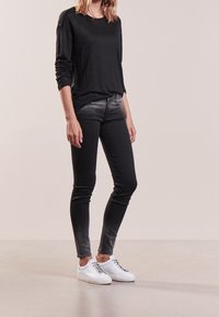 Czarna koszula z długim rękawem w połączeniu z ciemnoszarymi dżinsami, które mają stopniowe przetarcie. Białe sneakersy dopełniają stylizację, charakteryzując się gładką strukturą.